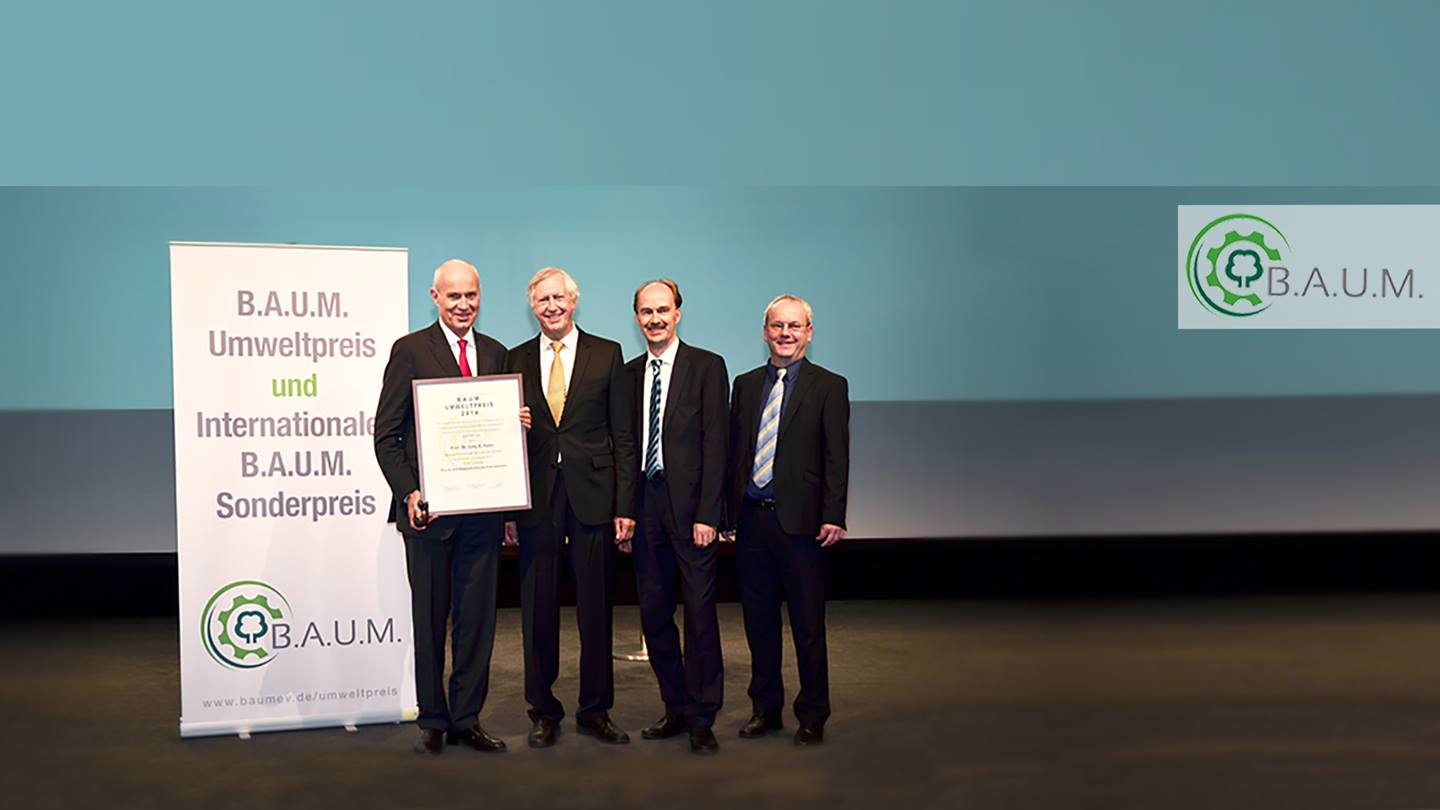 Vier Herren im Anzug stehen auf einer Bühne. Daneben ein Banner mit der Aufschrift B.A.U.M. Umweltpreis 2014. Der Herr links ist Prof. Dr. Götz Rehn. Er hält seine Auszeichnung in der Hand.